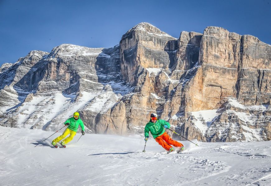 Sciatori in pista con vista sul Sas dla Crusc