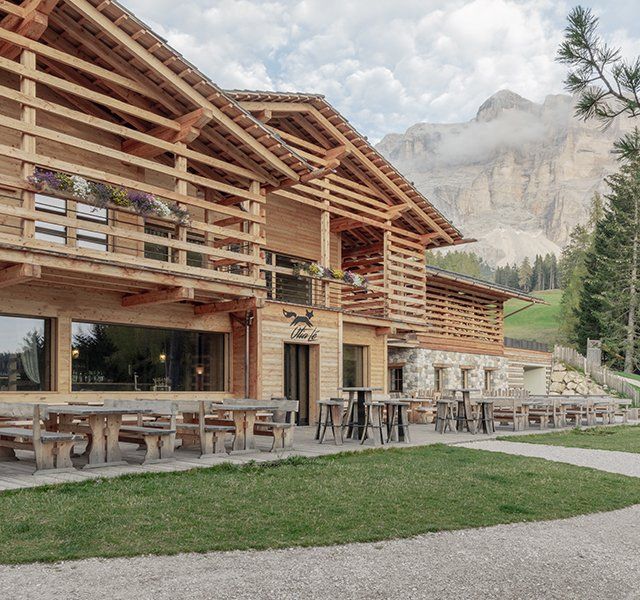 La facciata in legno e i tavoli all'esterno del Rifugio Ütia Lé d'estate